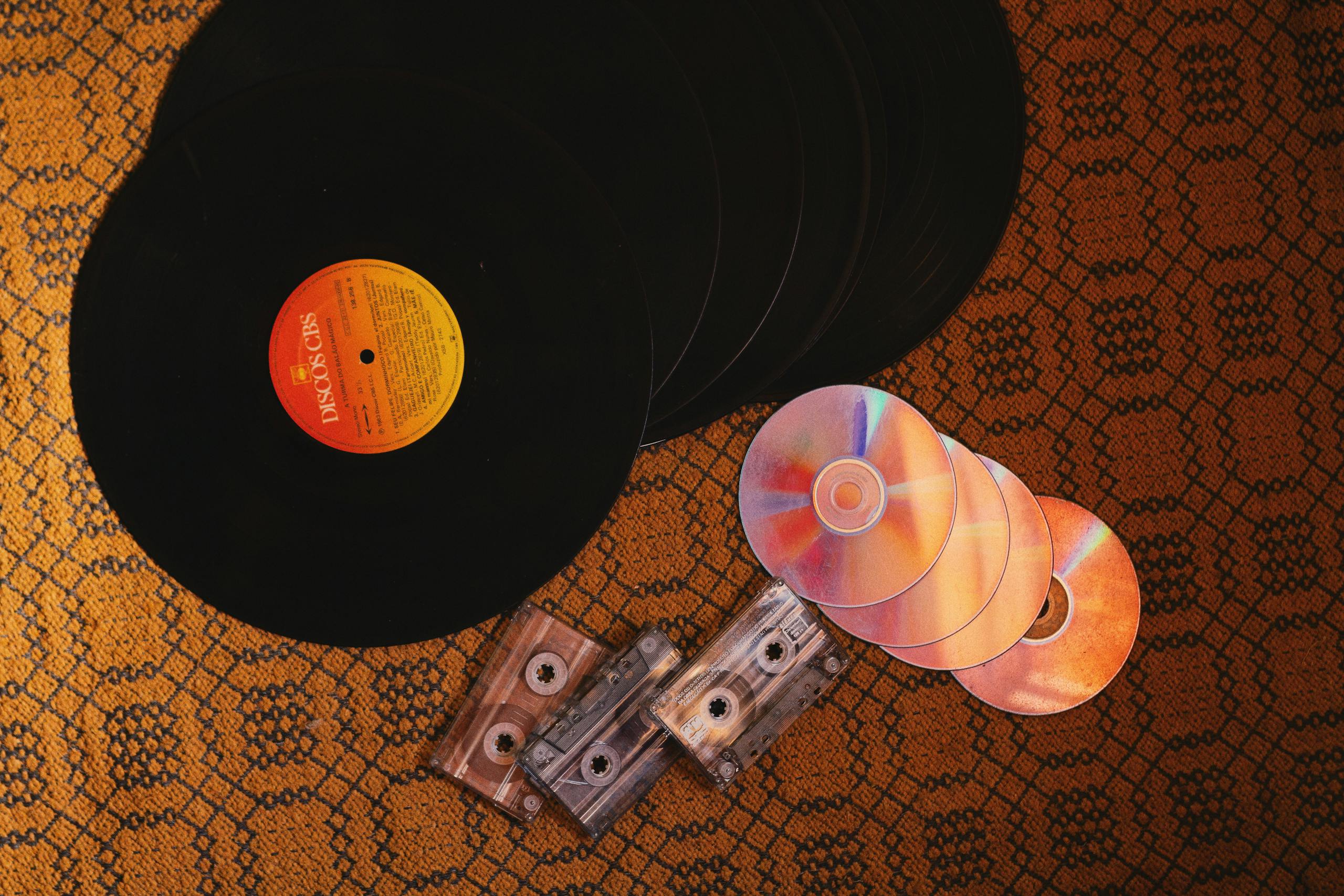 A nostalgic collection of retro music formats including vinyl records, CDs, and cassettes on a patterned surface.