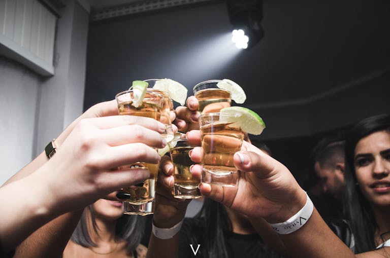 Friends raising tequila shots with lime in a lively indoor bar setting.